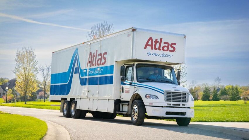 An Atlas Van Lines moving truck drives along a residential street.