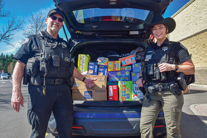 School resource officers Phil Anderson of Battle Ground, left, and Chelsea Quiggle of the Clark County Sheriff&rsquo;s Office stand beside a patrol vehicle filled with donated snacks during the Cram the Cruiser event on Saturday, March 28, at the Battle Ground Fred Meyer parking lot. The inaugural drive collected thousands of items to support student food pantries at local high schools.