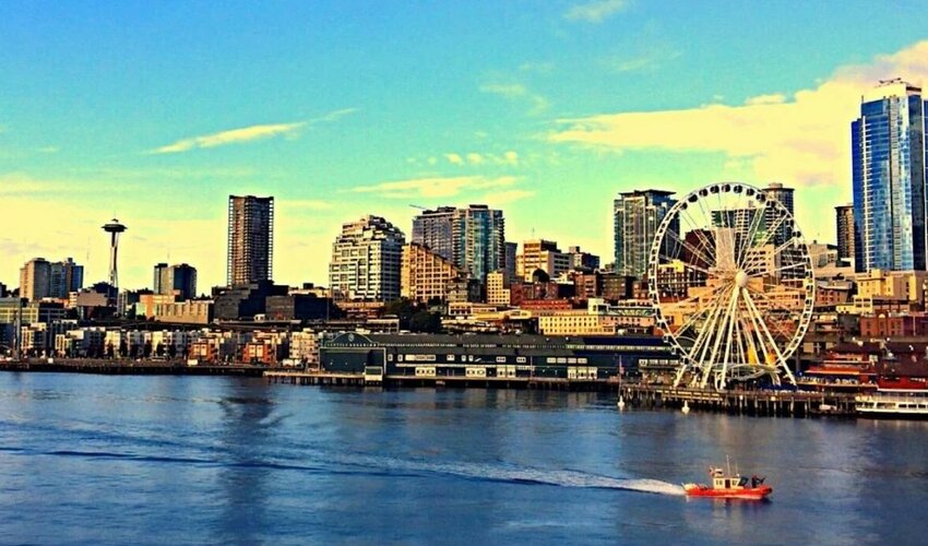 The Seattle skyline is seen with the Space Needle and a ferris wheel near the waterfront.