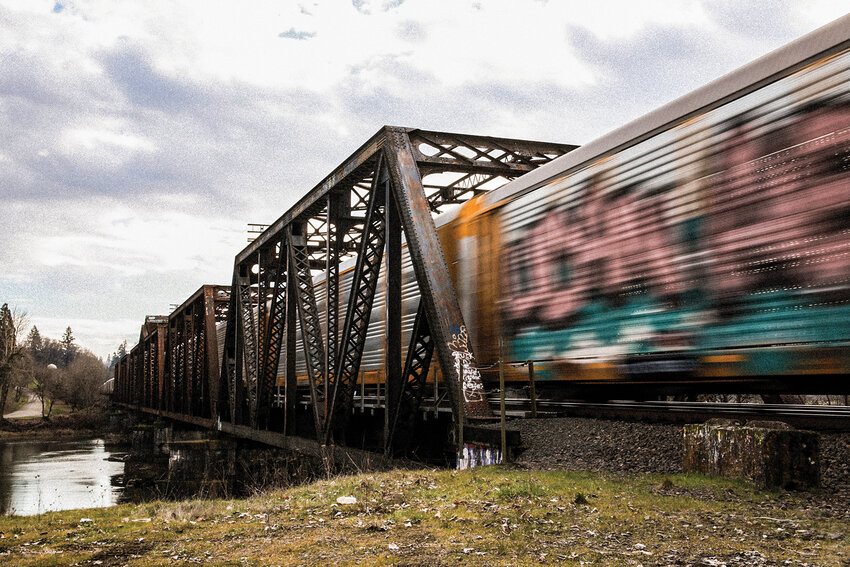 The &ldquo;Ghost Bridge&rdquo; south of Woodland tagged with graffiti across a murky stretch of the Lewis River while a train covered in graffiti crosses.