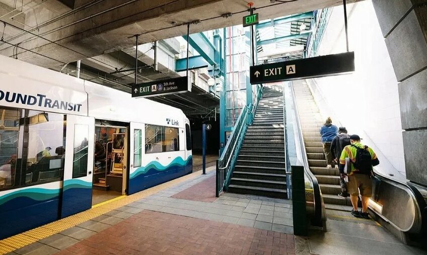 A Sound Transit Link light rail train is stopped at a station as riders use the stairs and escalator to exit.
