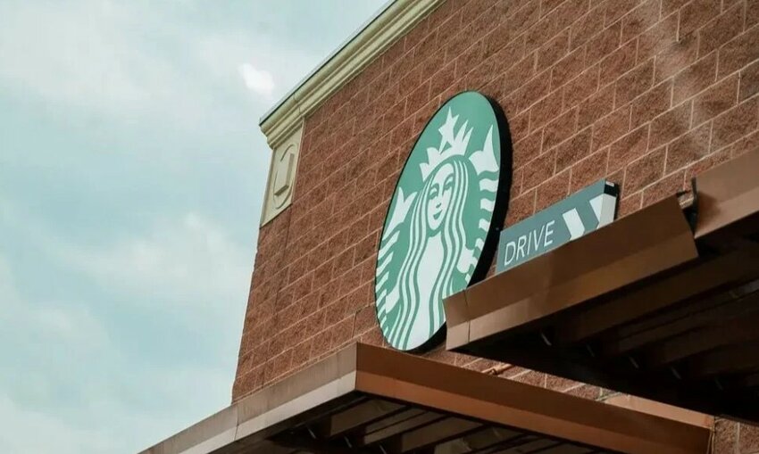 A Starbucks Coffee sign and drive-thru sign are displayed on the side of a brick building.