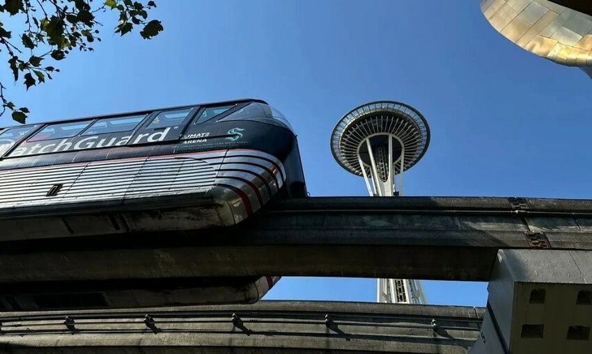 A Seattle monorail train passes on an elevated track near the Space Needle on a clear day.