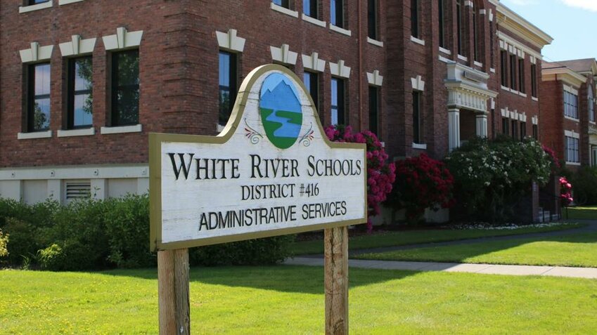 A sign for the White River School District with the district office behind.