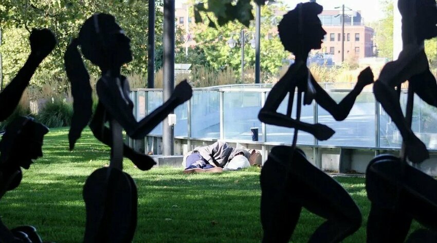 A homeless person rests on the grass near the Numerica Skate Ribbon at Riverfront Park in Spokane, Wash.