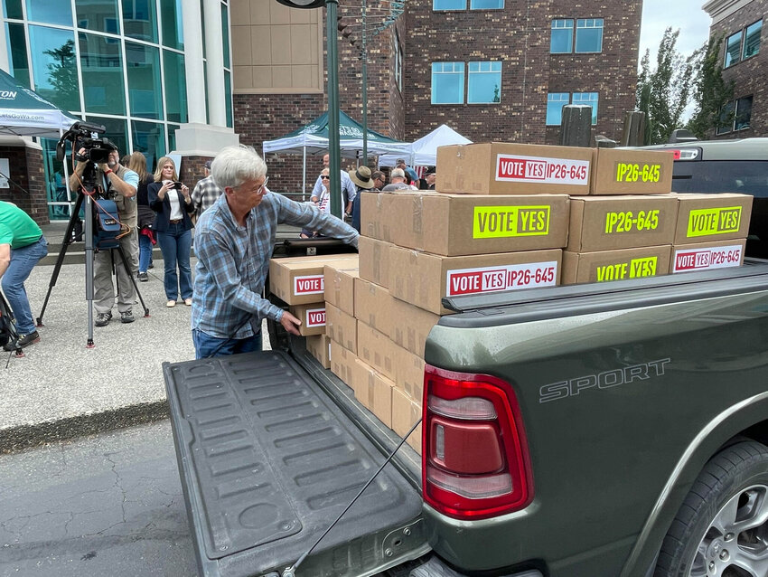 A volunteer for Let's Go Washington unloads boxes of petitions for Initiative 645 that were turned in to the secretary of state's office on July 2, 2026. The measure seeks to repeal Washngton's new income tax on high earners. Differences on how to describe the fiscal effects of the measure passing has sparked legal fights that could reach the state Supreme Court.