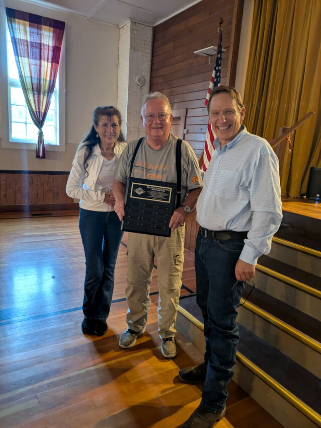 Sue and Wayne Sutton, left, stand with Tim Hadler and a plaque recognizing future recipients of the Sutton Forestry/Veterans Scholarship Fund, an educational aid fund established by Hadler through GUMI CAMP USA.