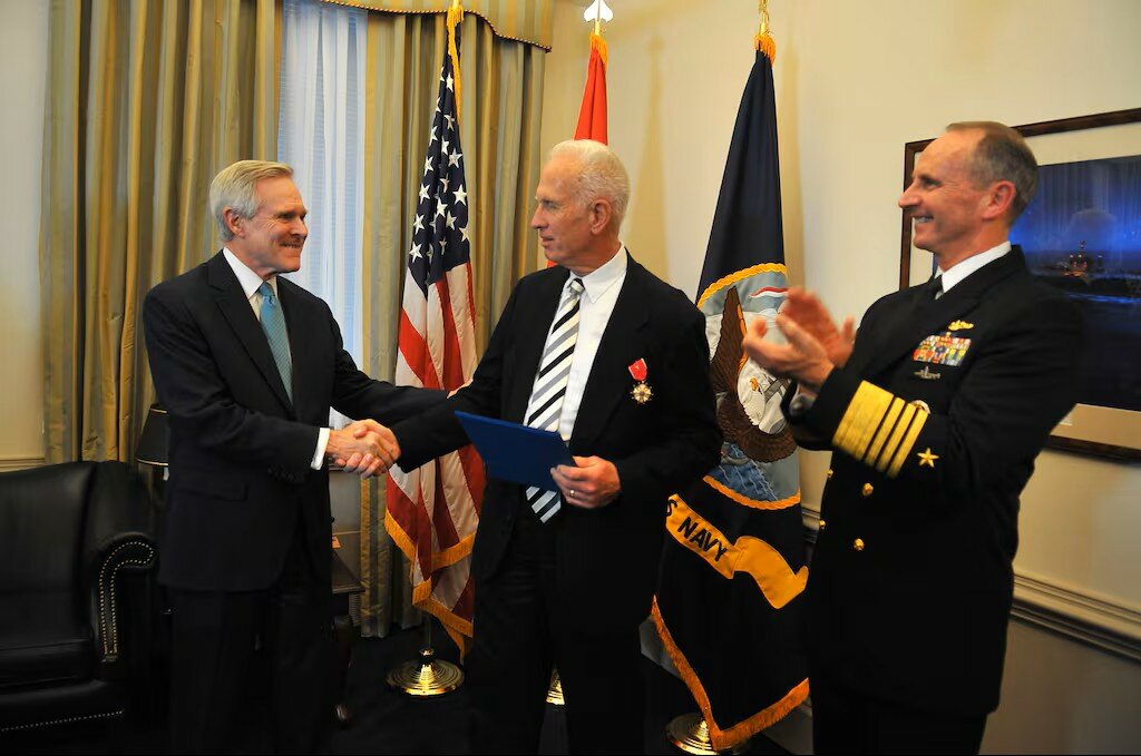 Secretary of the Navy Ray Mabus and Chief of Naval Operations Adm. Jonathan Greenert present the Legion of Merit posthumously to Lt. Cmdr. Herbert Claudius for his actions on July 30, 1942. His son, Herbert Gordon Claudius Jr., center, accepted the award on behalf of his late father during a ceremony at the Pentagon Dec. 16. 2014. The actions of Lt. Cmdr. Claudius as commanding officer of PC-566 resulted in the sinking of enemy submarine U-166.